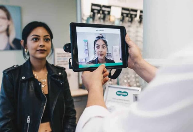 A woman sits in front of a tablet, where the optician is using the Specsavers app to assist in the appointment